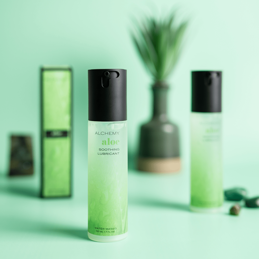 Alchemy Aloe: Hydrating Water-Based Personal Lubricant bottles with live plant and stones on green background