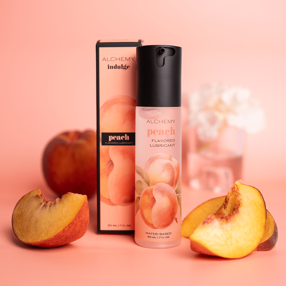 Alchemy Indulge: Peach Flavored Personal Lubricant bottle and box with peach slices and pink background