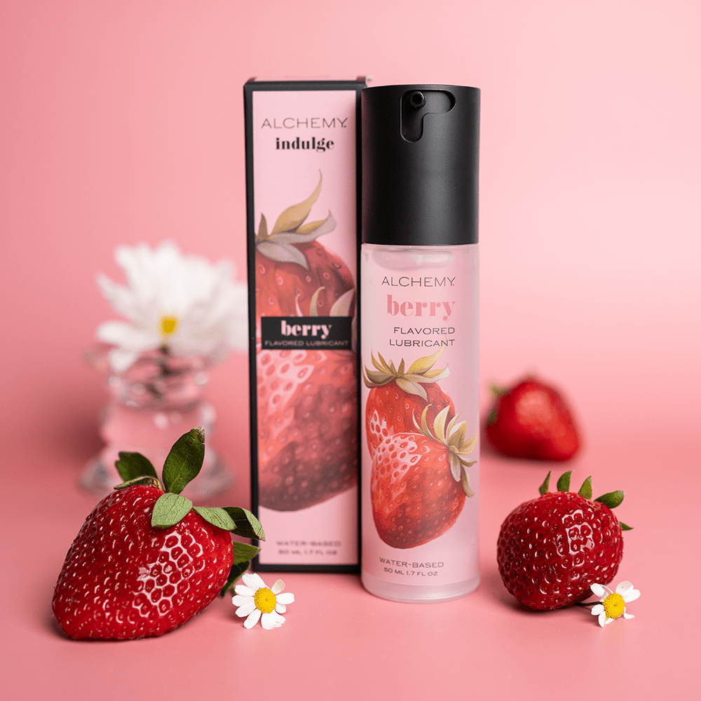 Alchemy Indulge: Strawberry Flavored Personal Lubricant bottle and box with fresh strawberries and pink background