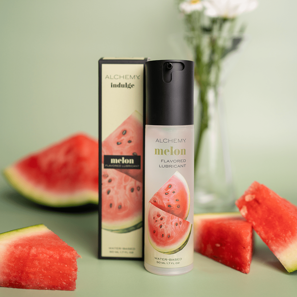 Alchemy Indulge: Watermelon Flavored Personal Lubricant bottle and box with fresh watermelon slices and green background