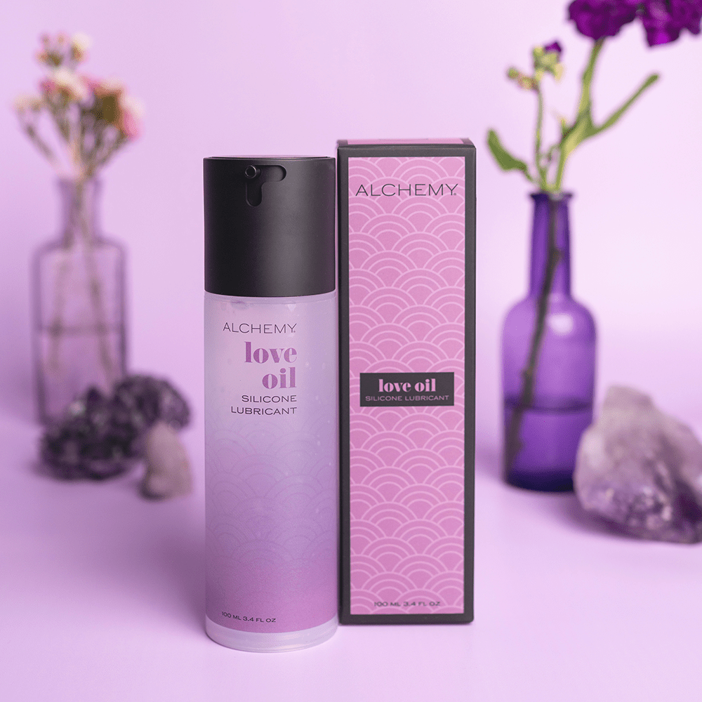 Alchemy Love Oil: Silicone-Based Personal Lubricant bottle and box with plants in vases and purple background