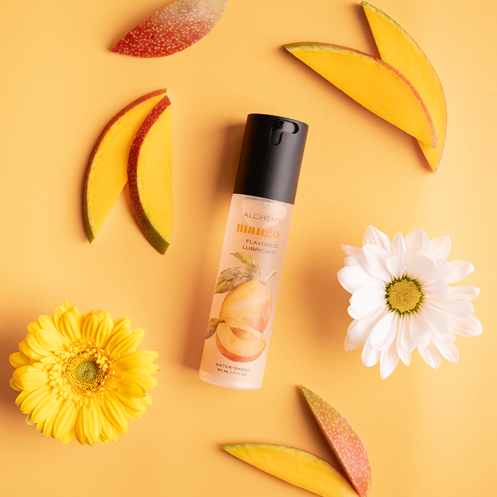 Alchemy Indulge: Mango Flavored Personal Lubricant bottle with mango slices and flowers