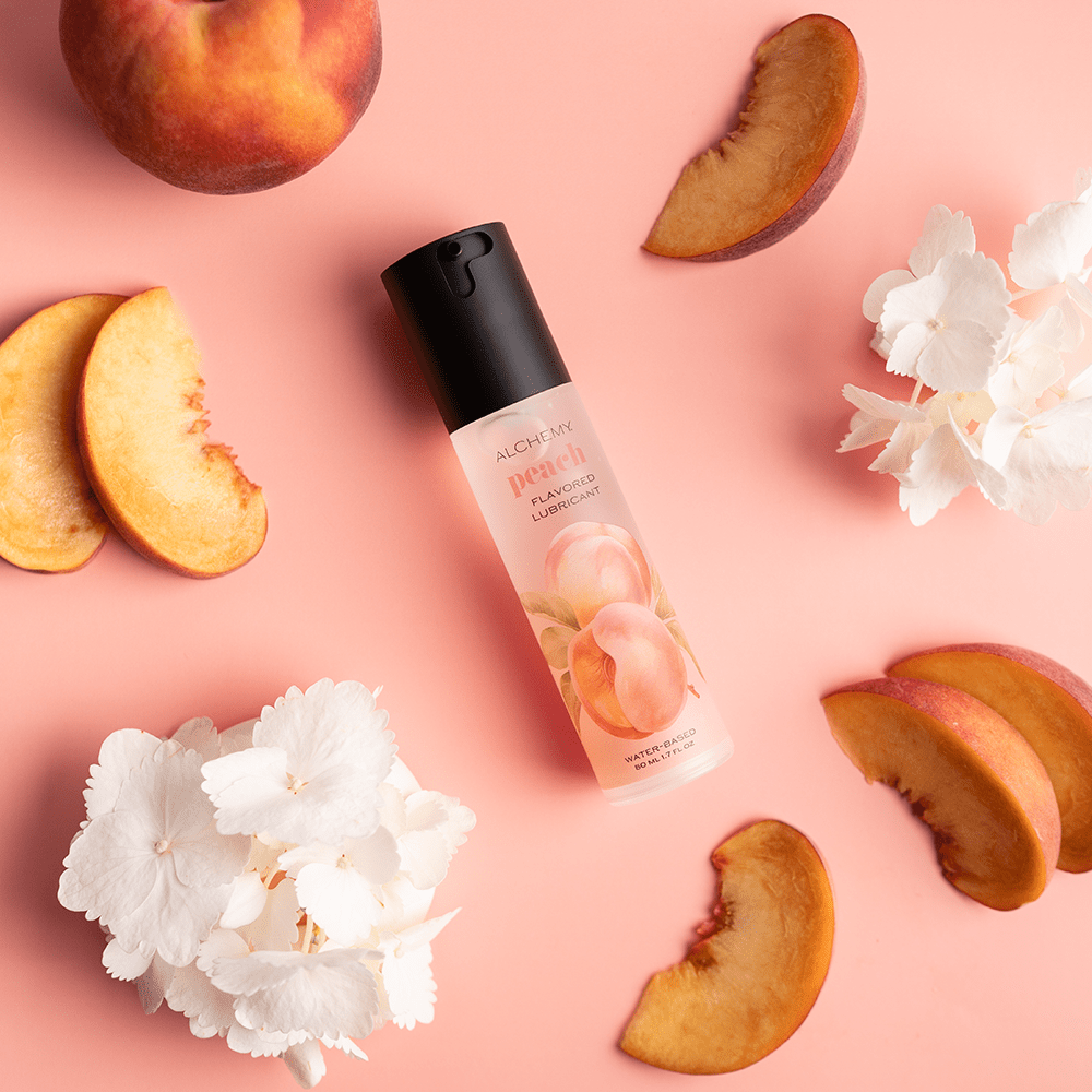 Alchemy Indulge: Peach Flavored Personal Lubricant bottle with peach slices and flowers