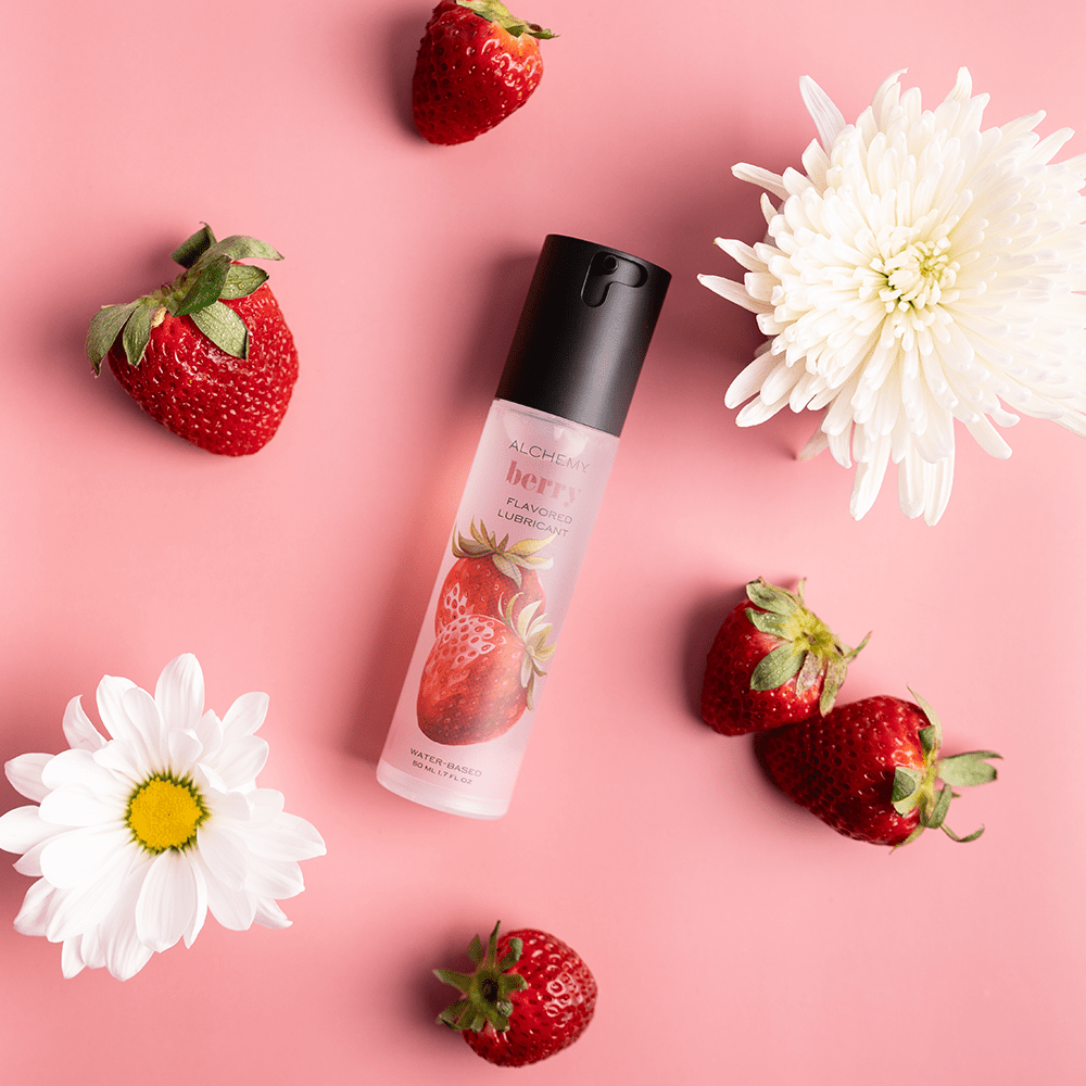 Alchemy Indulge: Strawberry Flavored Personal Lubricant bottle with fresh strawberries and flowers