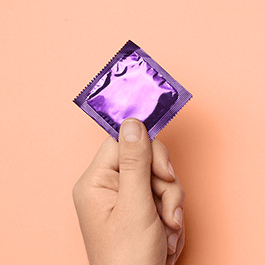 Person's hand holding condom with purple wrapper