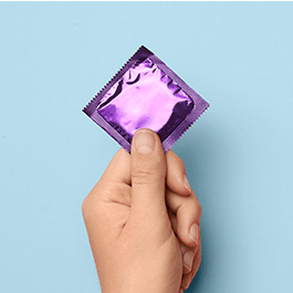 Person's  hand holding condom with purple wrapper
