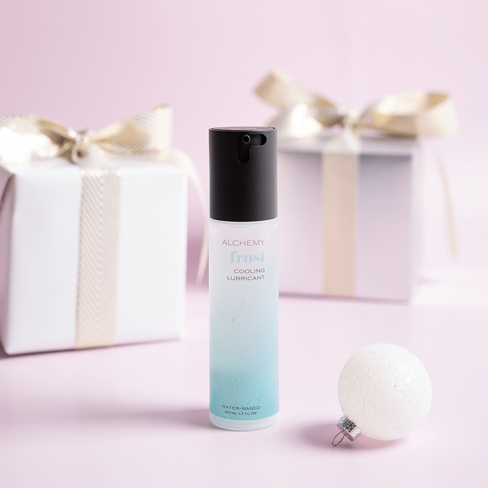 Alchemy Frost: Water-Based Cooling Personal Lubricant with holiday gift boxes, ornaments, and light pastel background