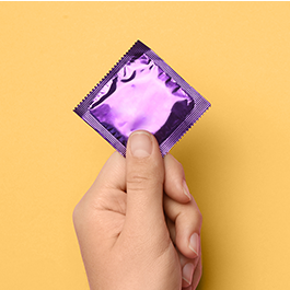 Person's hand holding condom with purple wrapper