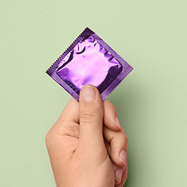 Person's hand holding condom with purple wrapper