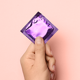 Person's hand holding condom with purple wrapper