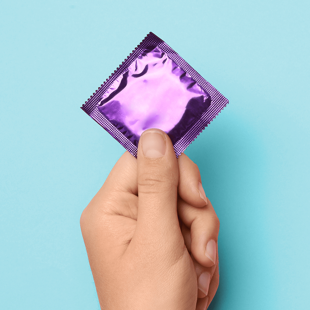 Alchemy Love Blend: Hybrid Personal Lubricant – person's hand holding condom with purple wrapper