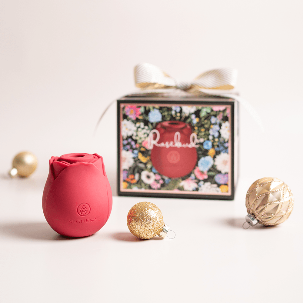 Alchemy Rosebud Luxury Air-Pulse Massager Vibrator with holiday gift boxes, ornaments, and light pastel background