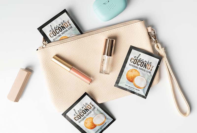 Alchemy Cleanse Coconut Scented Wipes top view with purse and makeup accessories on a white surface