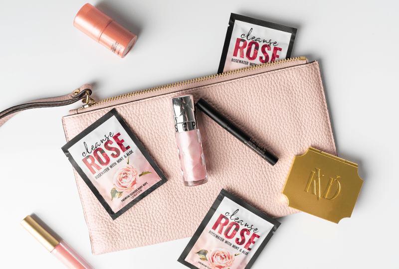 Alchemy Cleanse Rosewater Scented Wipes top view with purse and makeup accessories on a white surface