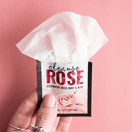 Alchemy Cleanse Rosewater Scented Wipes – woman's hand holding a single packet in front of a pink background