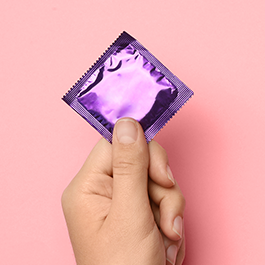 Person's  hand holding condom with purple wrapper