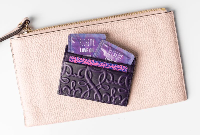 Alchemy Love Oil Silicone-Based Snap + Slide Single-Use Personal Lubricant Packets close-up shot of packets in feminine leather wallet