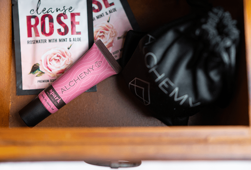 Alchemy Spark Female Arousal Gel 1oz tube in a wooden drawer with Alchemy Cleanse personal wipes and a Rosebud vibrator pouch with soft interior lighting